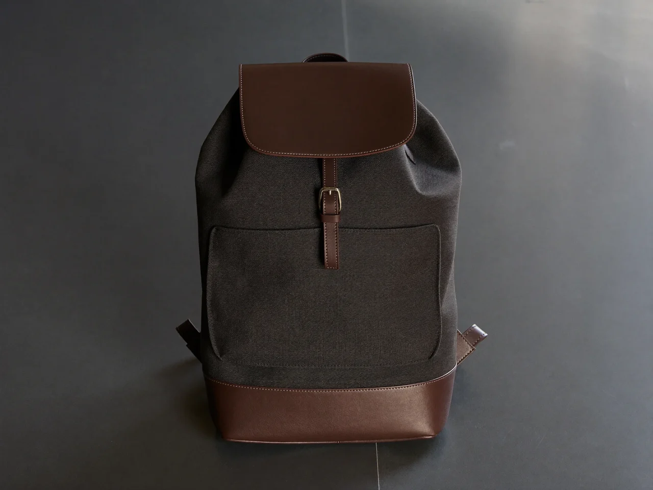 Minimalistischer Canvas-Rucksack mit Lederdetails steht aufrecht auf dunklem Studioboden