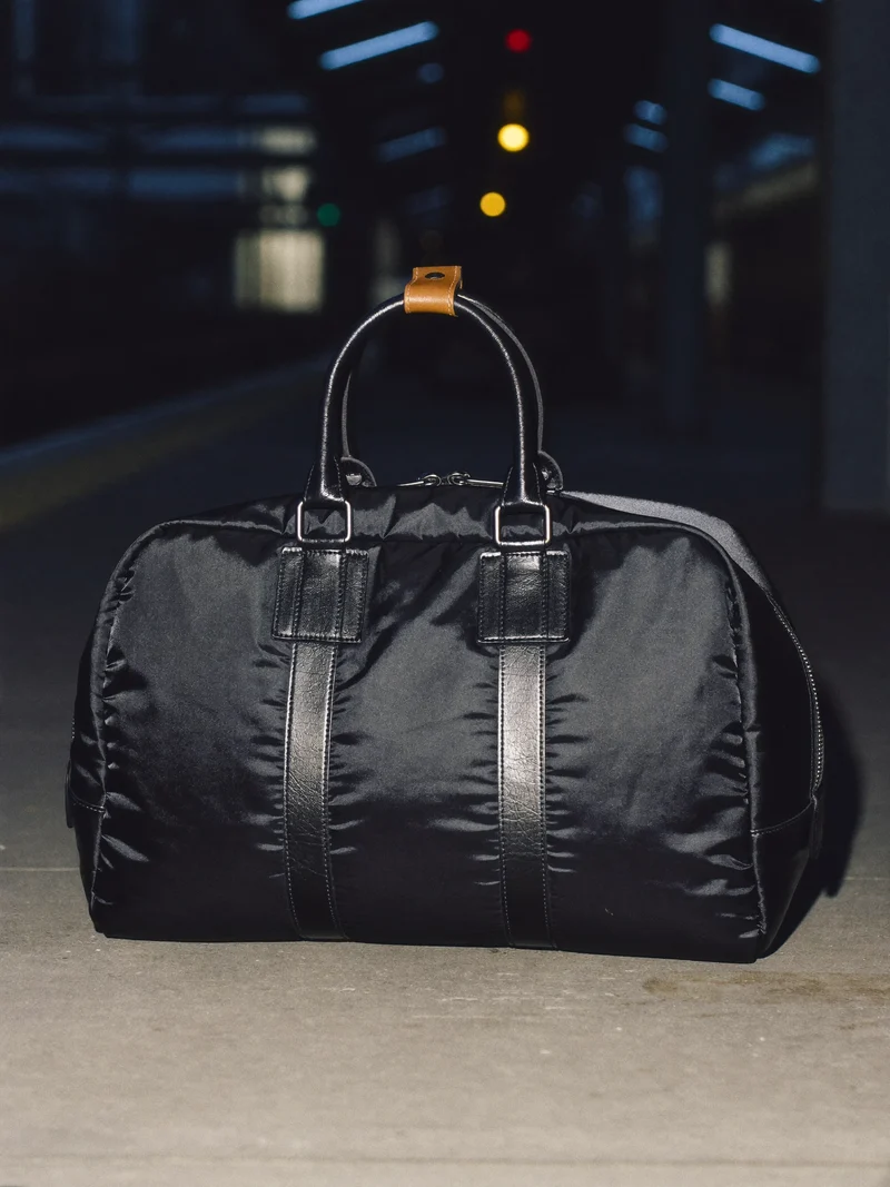 Schwarze Nylon-Reisetasche mit Lederhenkeln auf einem nächtlichen Bahnsteig